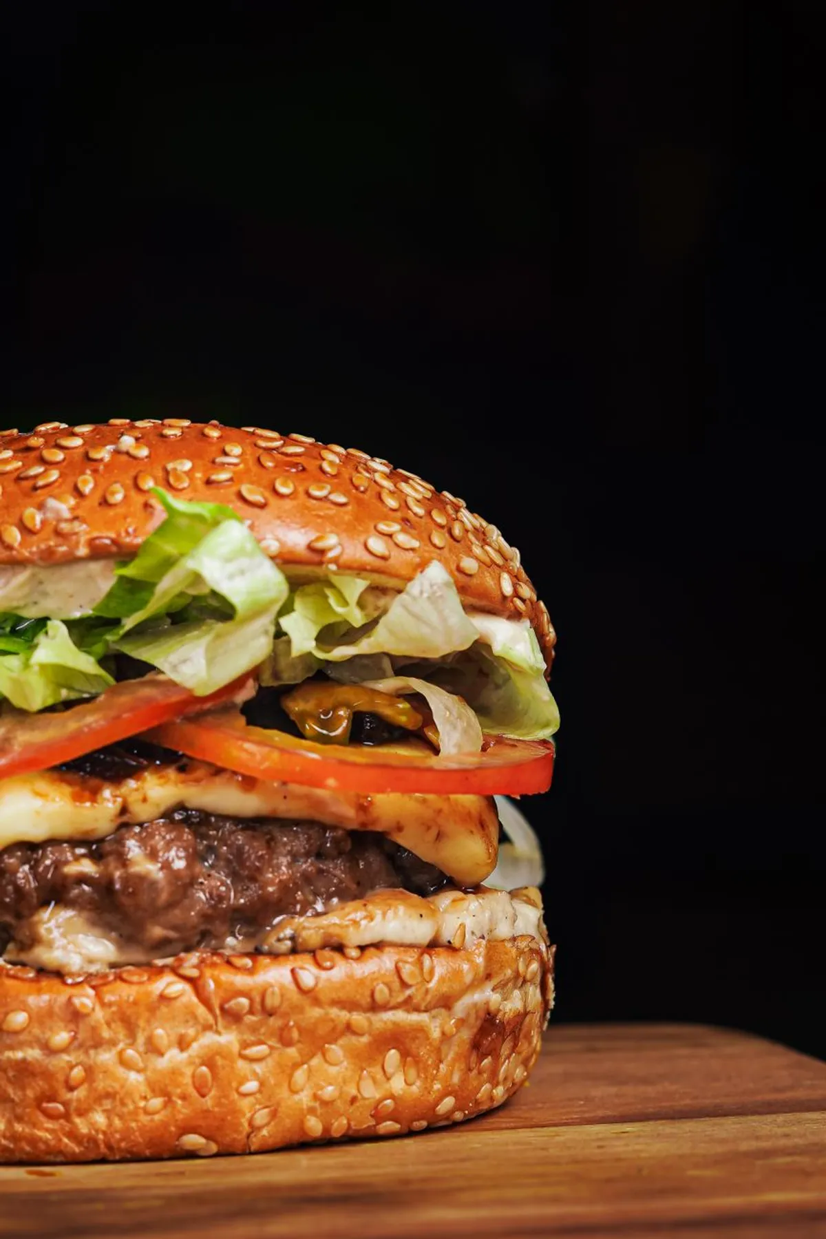 Hamburguesa en pan de sesamo con lechuga y tomate sobre tabla de madera