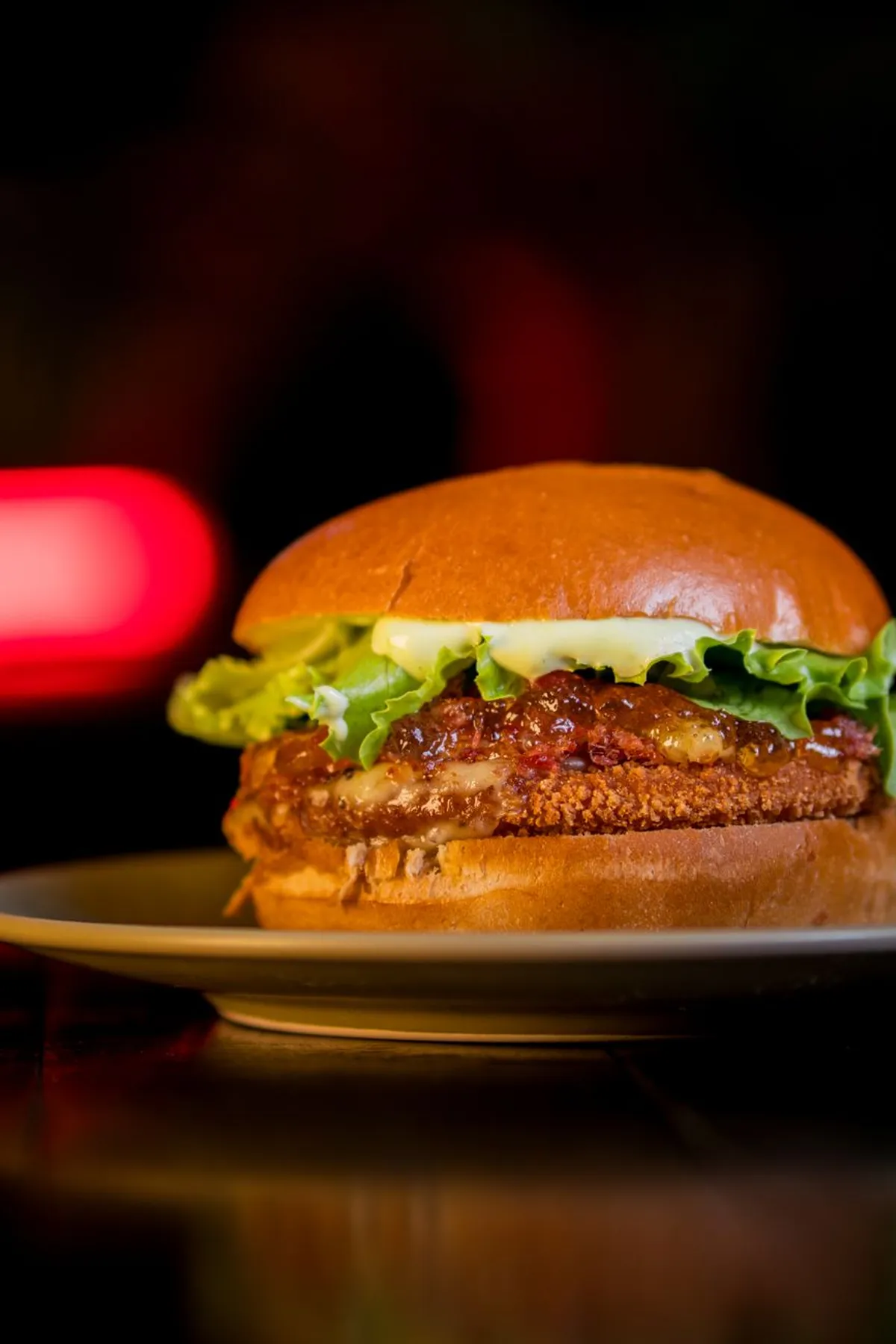 Hamburguesa con mermelada de chili y lechuga sobre fondo oscuro con luz roja