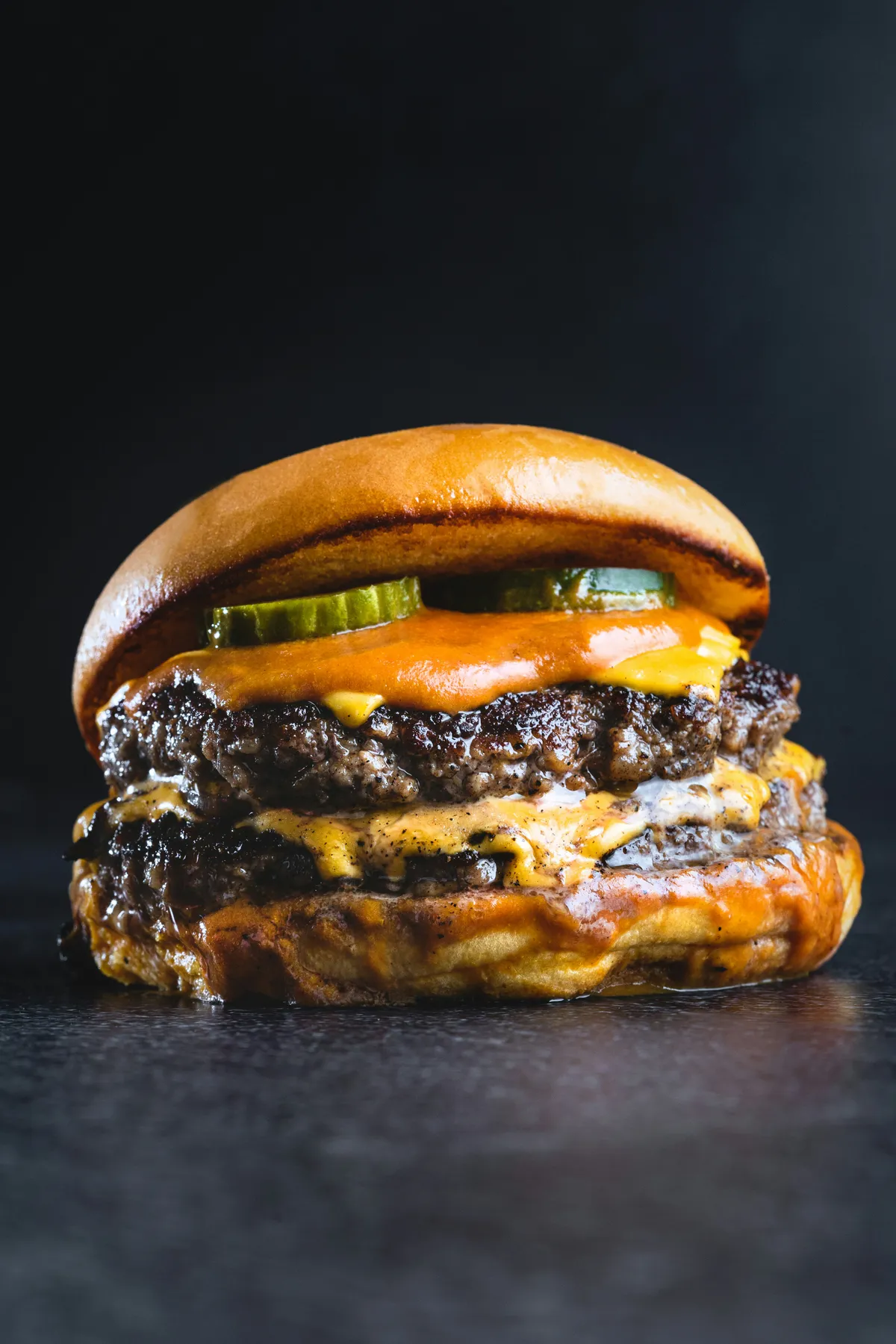 Hamburguesa doble con queso fundido sobre fondo oscuro