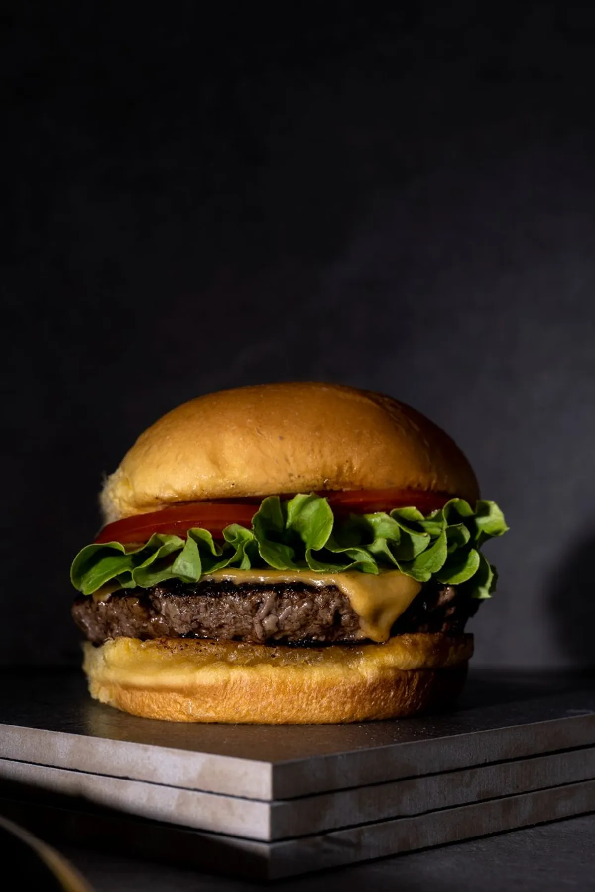 Hamburguesa sencilla con queso, lechuga y tomate sobre fondo oscuro