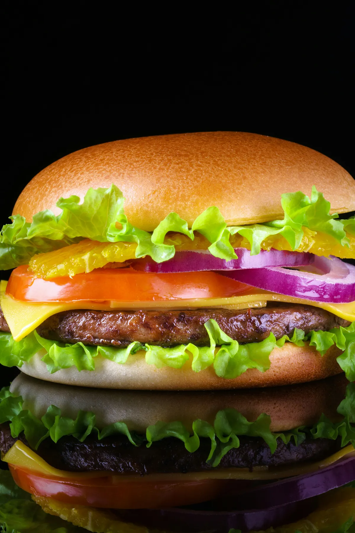 Cheeseburger con lechuga, tomate y cebolla sobre fondo negro